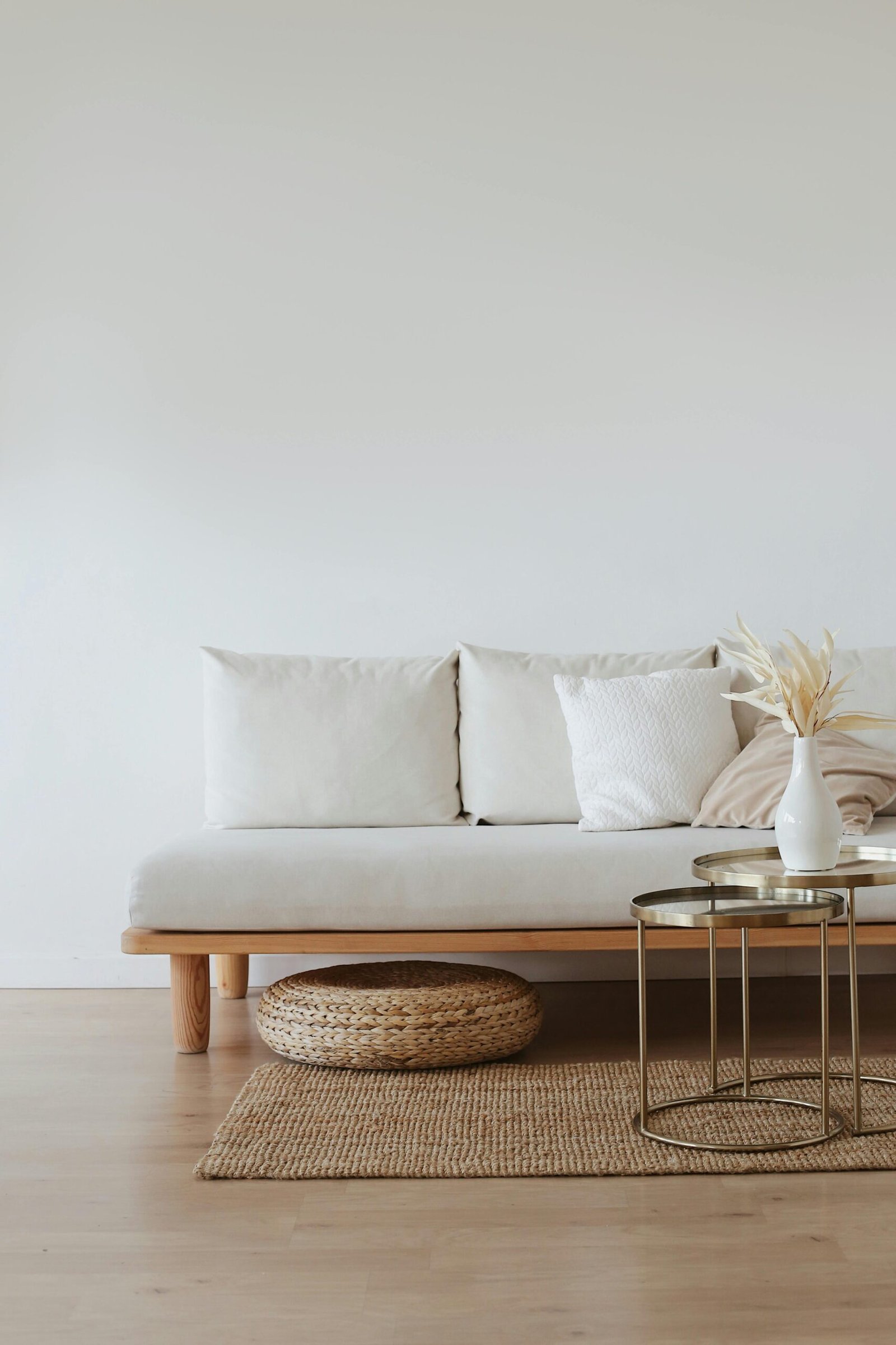 Home A chic minimalist living room featuring a white sofa with cushions, dried flowers in a vase, and a wooden floor.